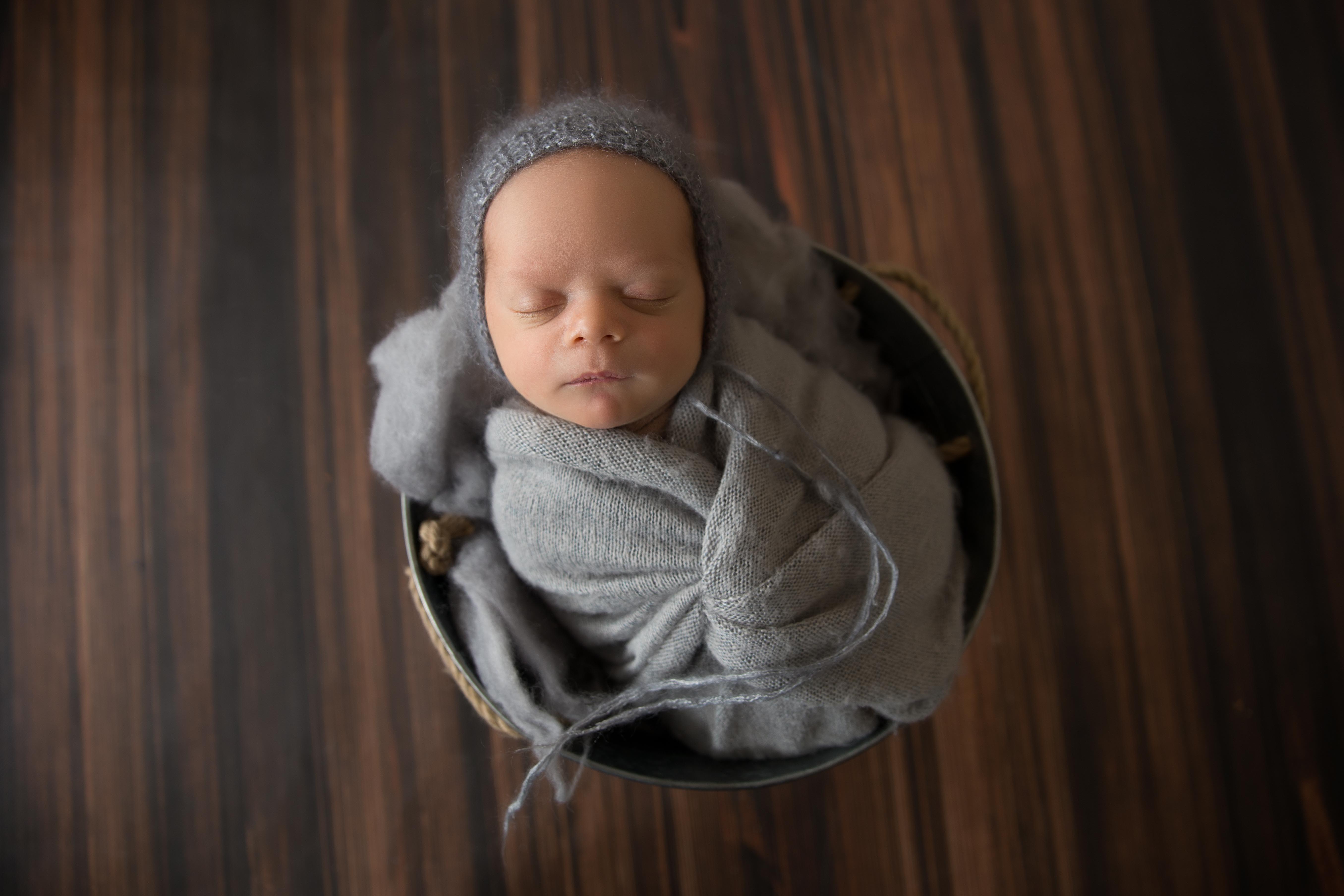 newborn baby wrapped in grey and placed in tin bucket for newborn photography 