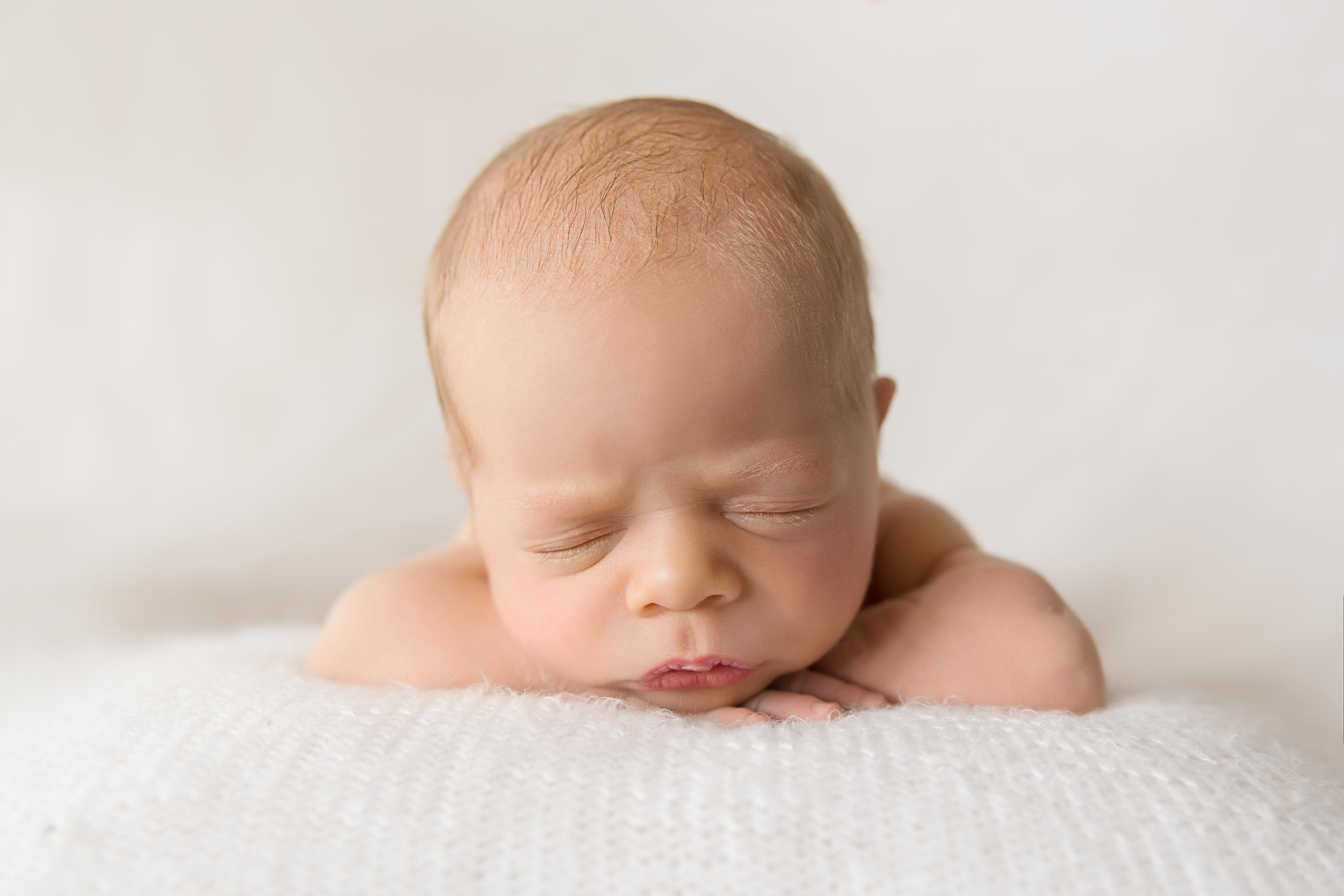 Newborn baby with head on hands 