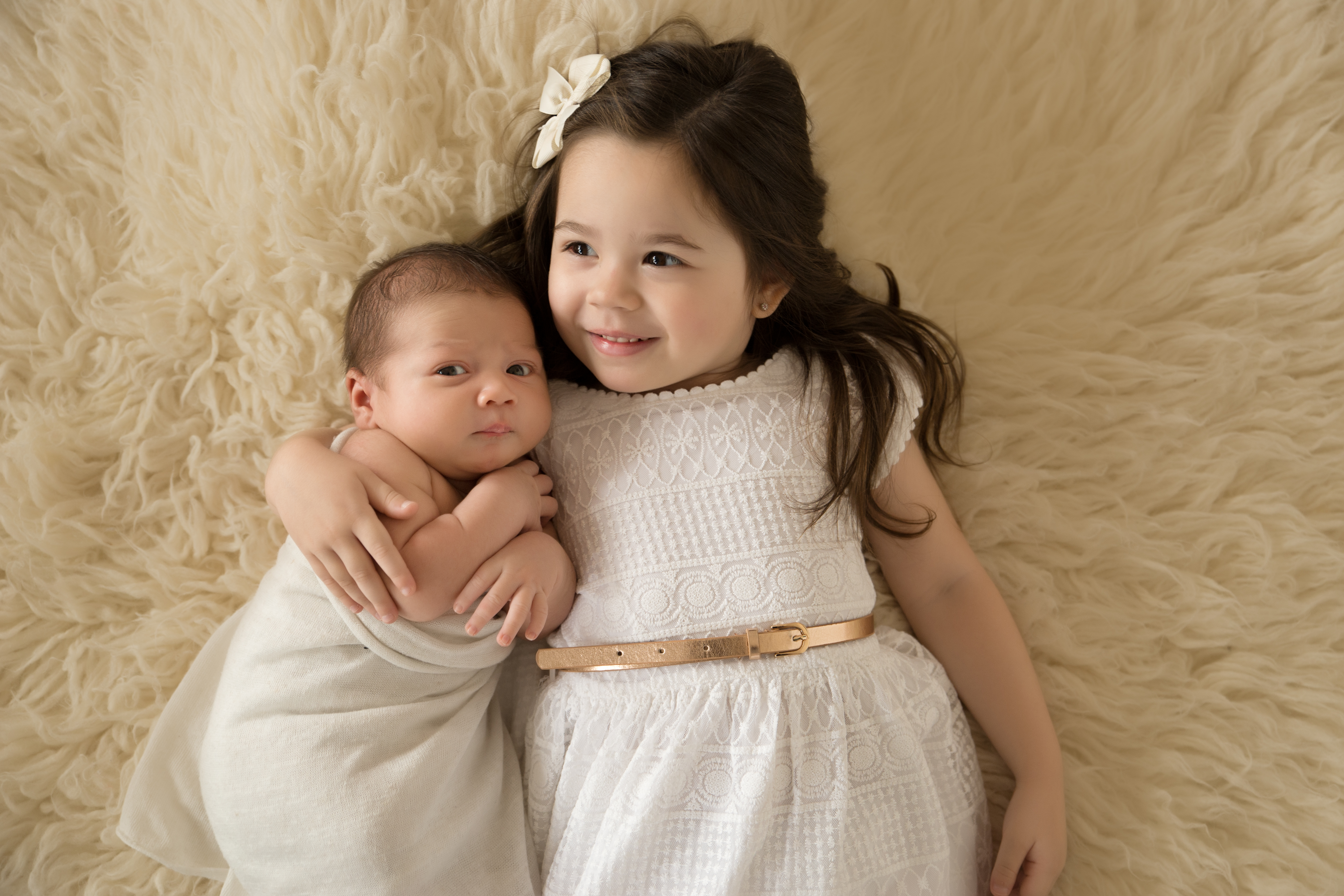 Beautiful photo of newborn baby and big sister laying together on a flokati 