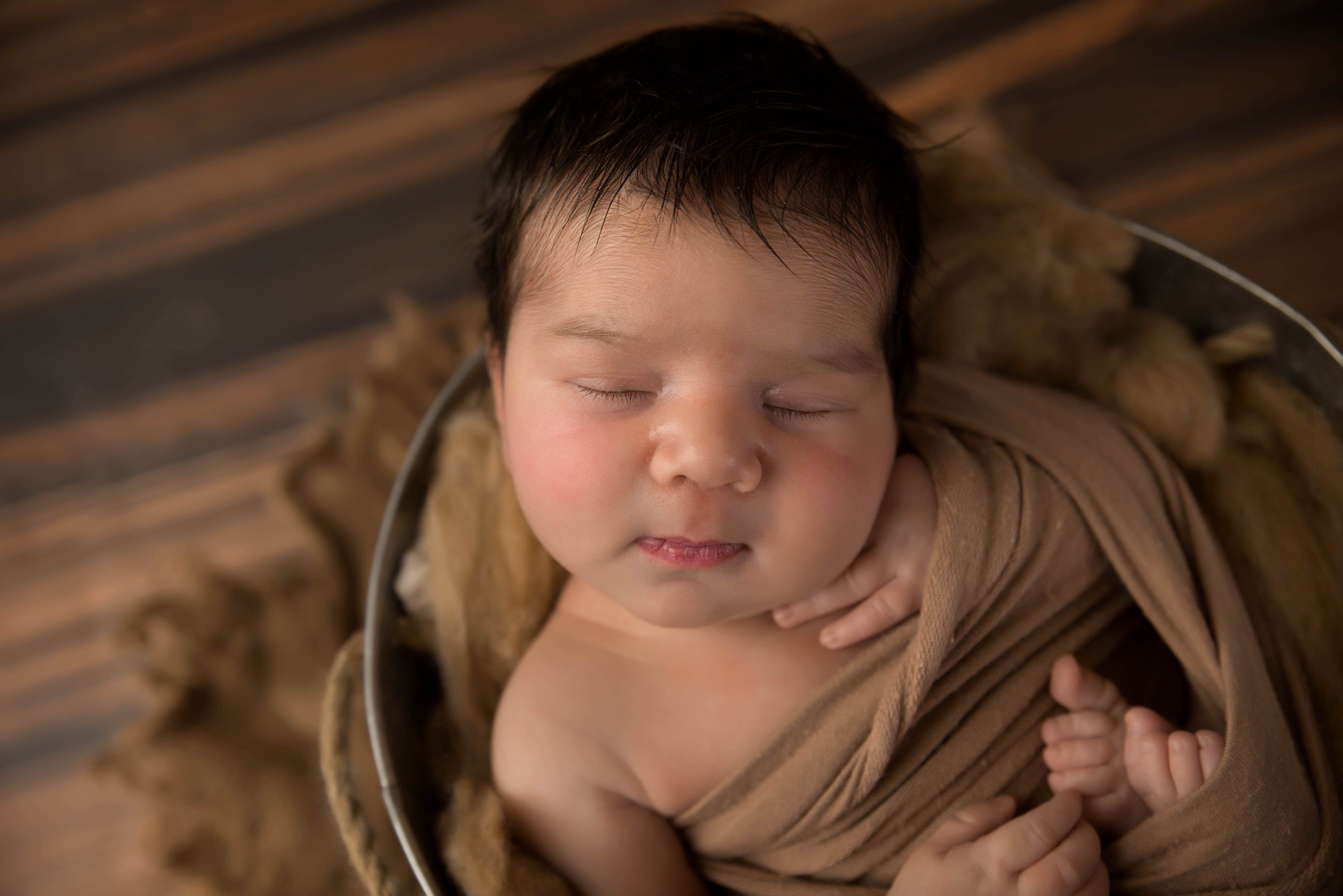 Newborn baby with hand on chest in silver bucket 