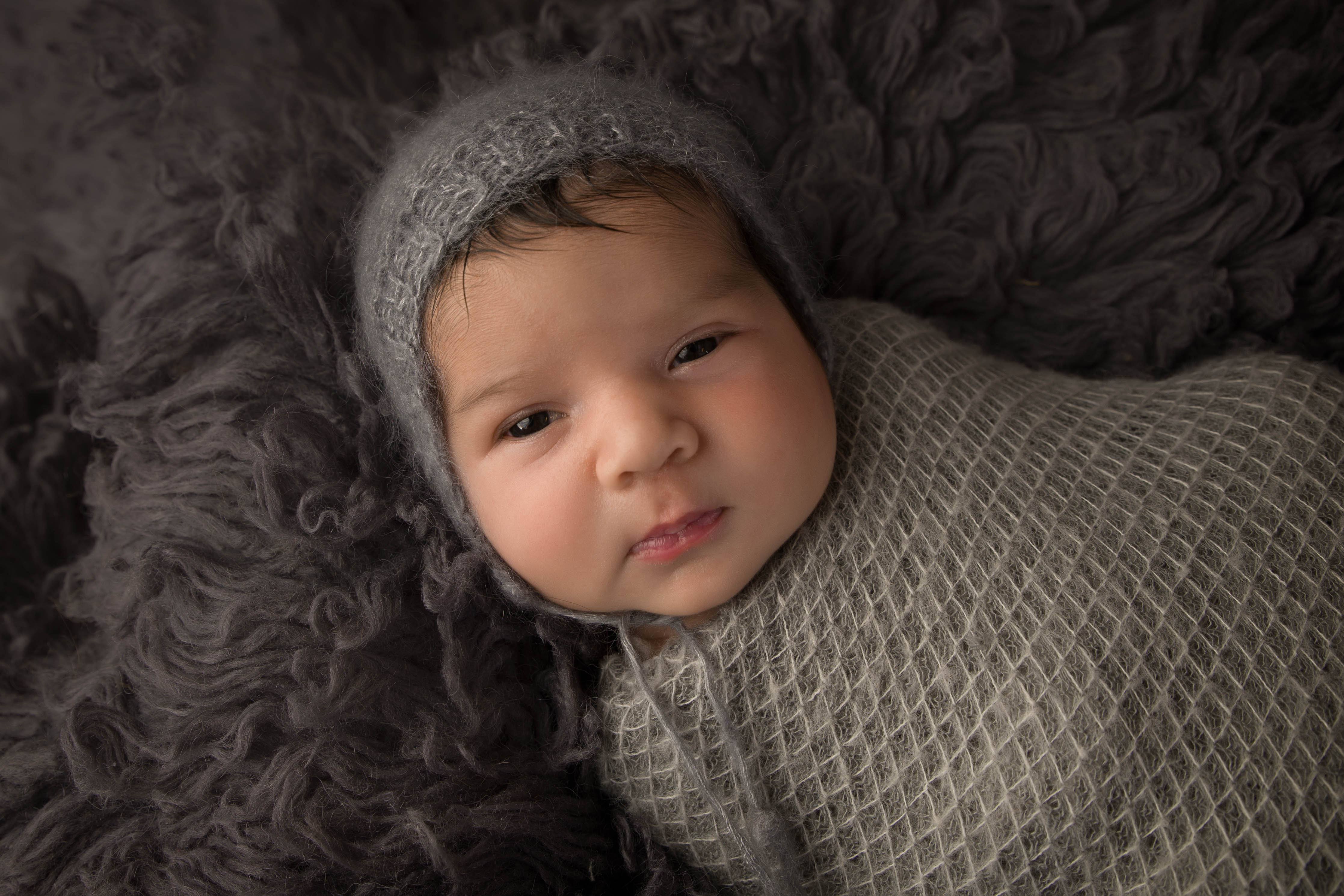 Newborn baby boy awake looking at camera in grey hat 