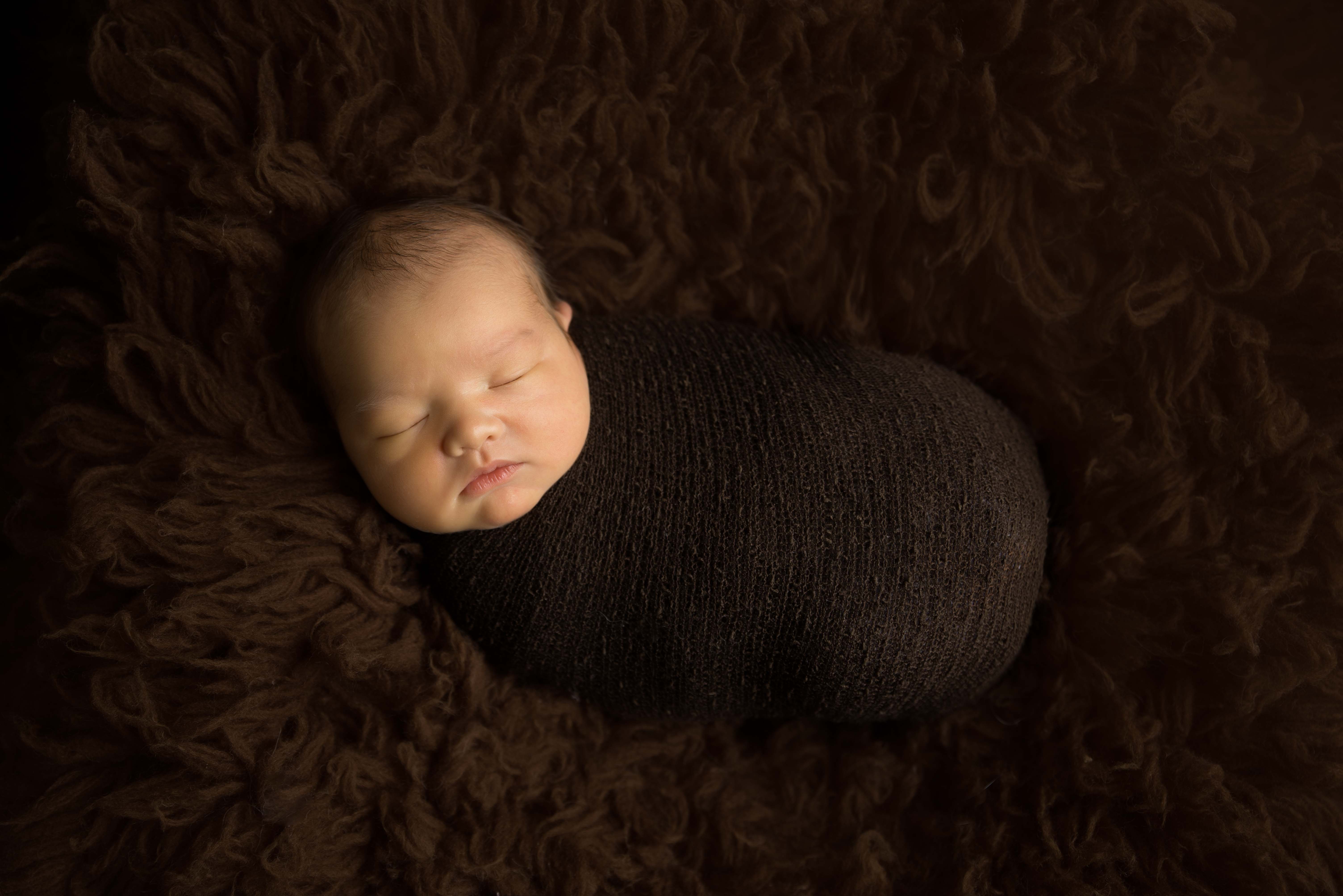 Newborn baby all wrapped up in brown wrap.