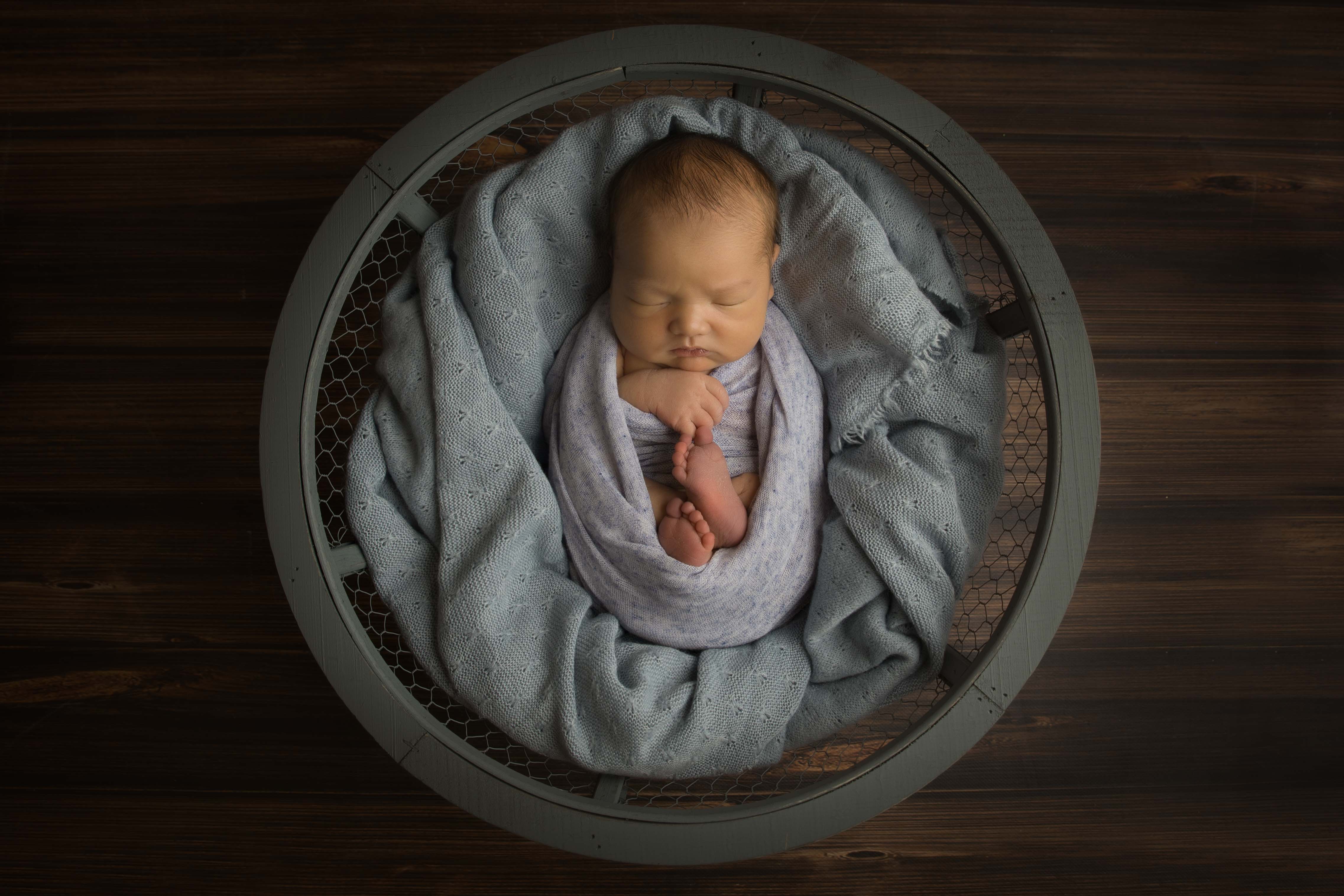 Baby all wrapped up and put in blue basket for baby photography.