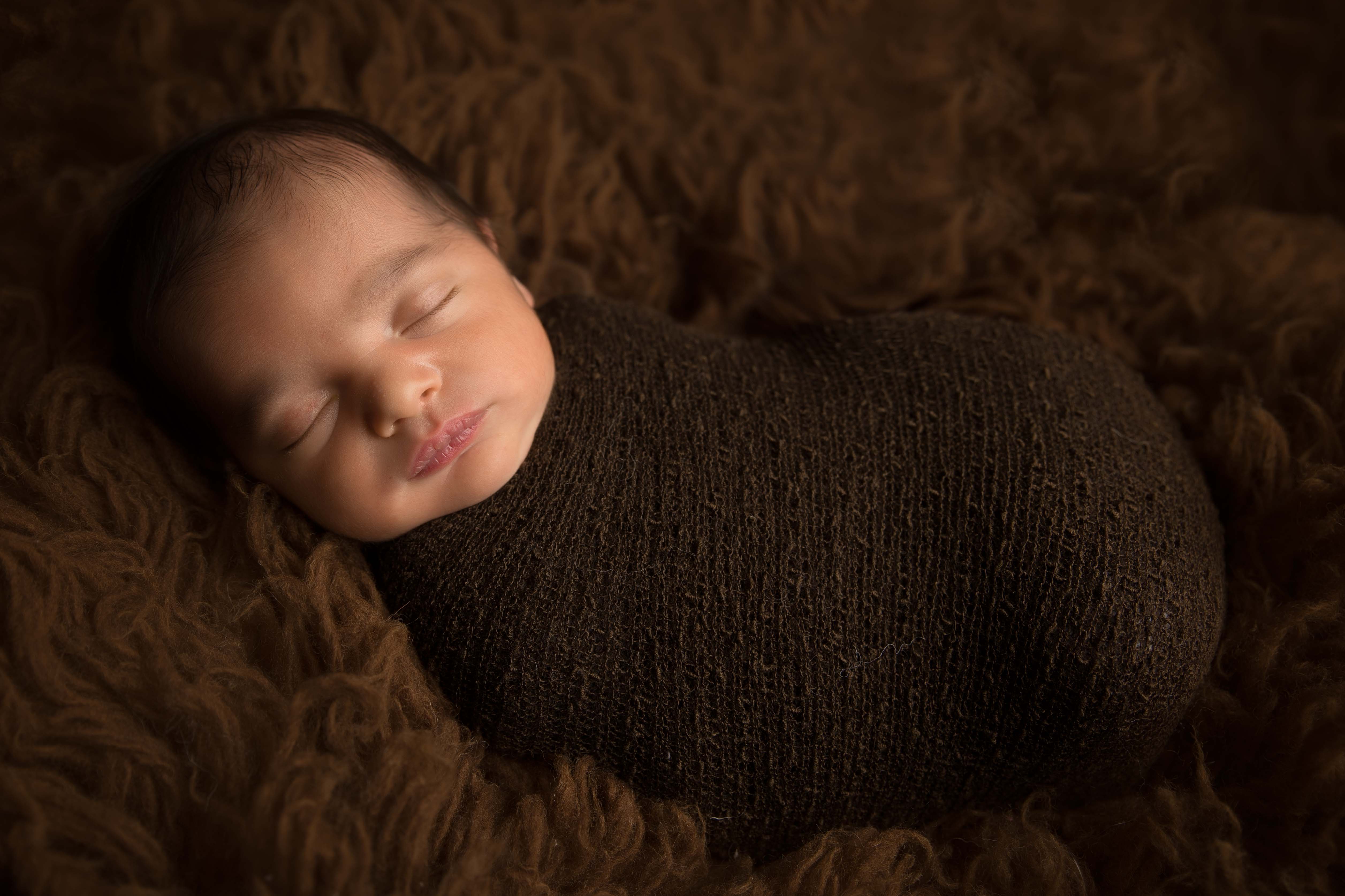 Baby all wrapped up on brown fur.