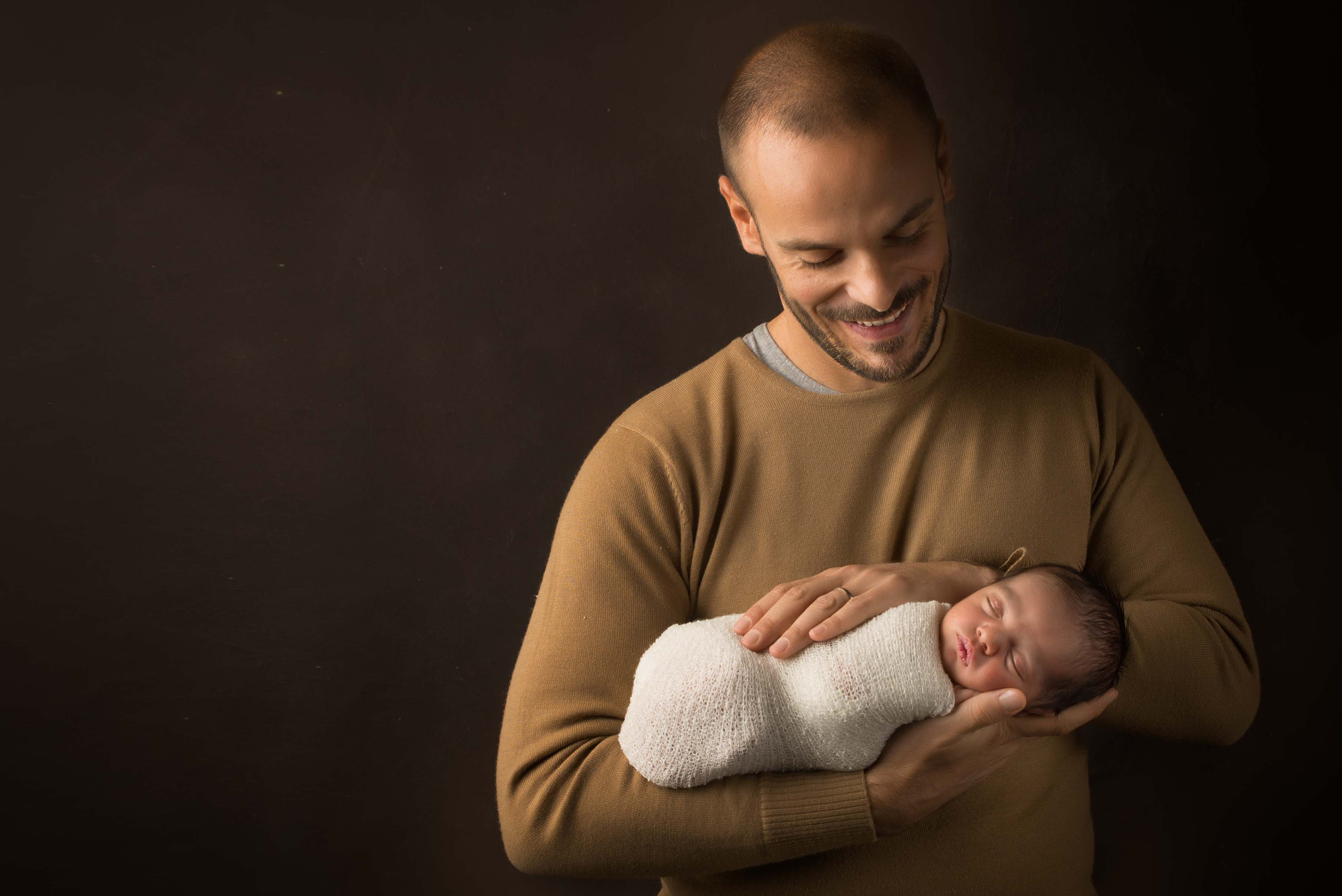 Dad looking down to newborn baby with big smile.