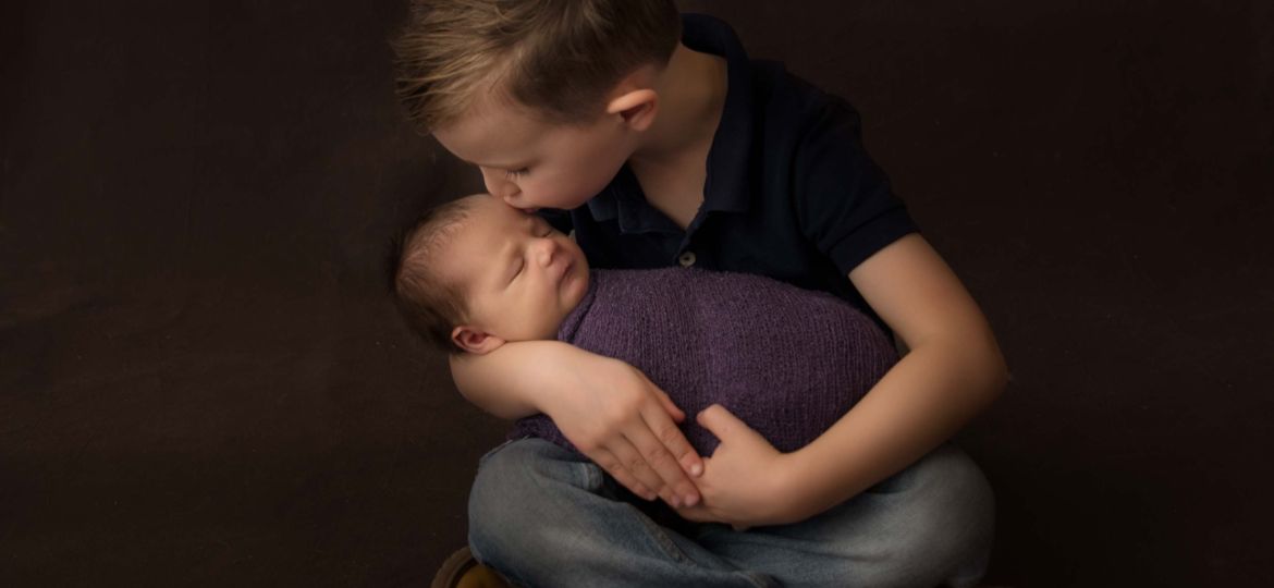 Big brother kissing his new baby sister for newborn photo.