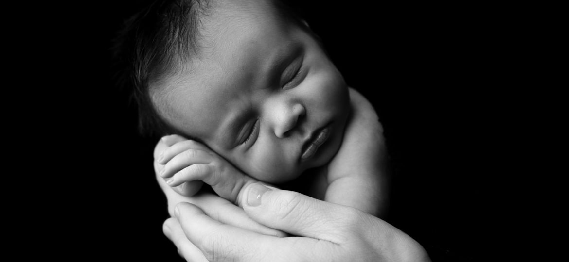 Newborn baby boy posed in dads hands for black and white photograph.